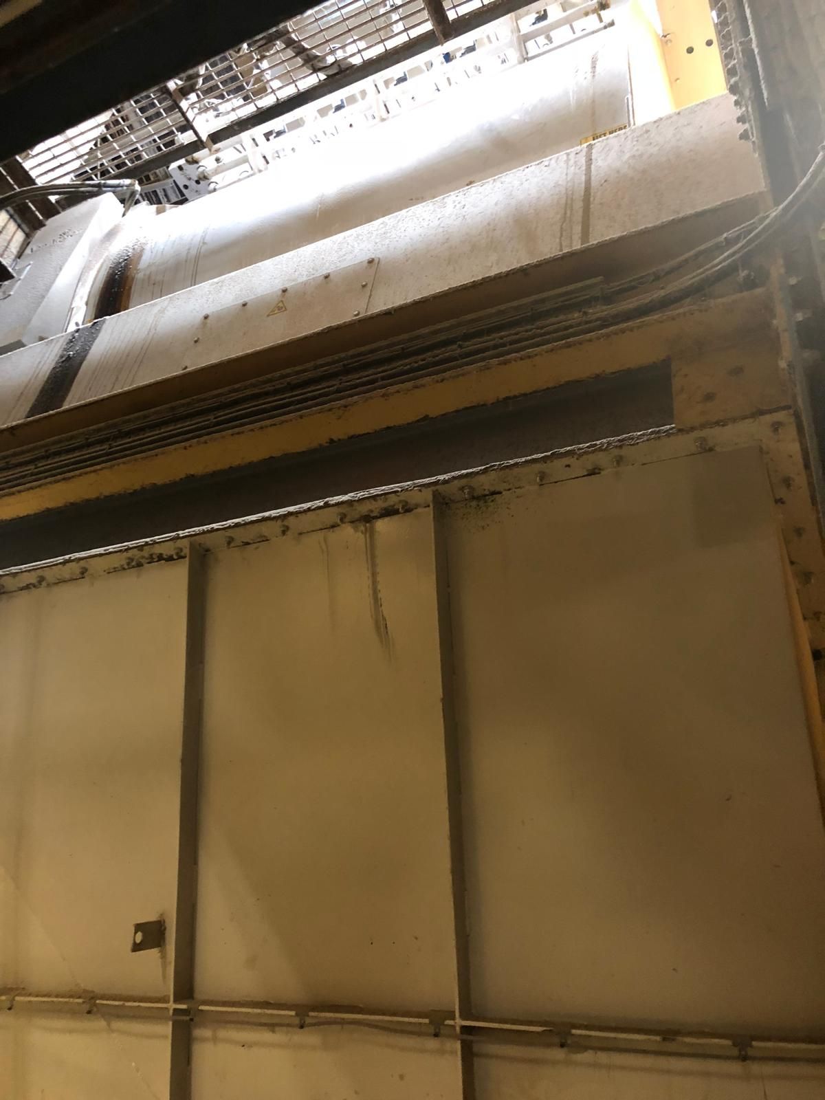 A low-angle view up at large dust-coated ductwork and tall painted plant panels high inside a feed mill building.