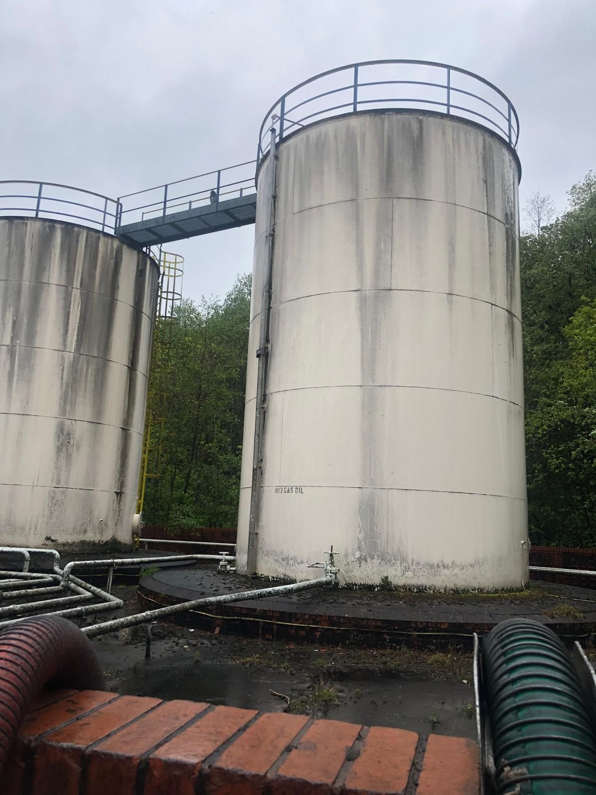Two vertical fuel storage tanks connected by an access gantry and a yellow caged ladder, one labelled No3 Gas Oil, seen from the bunded base.